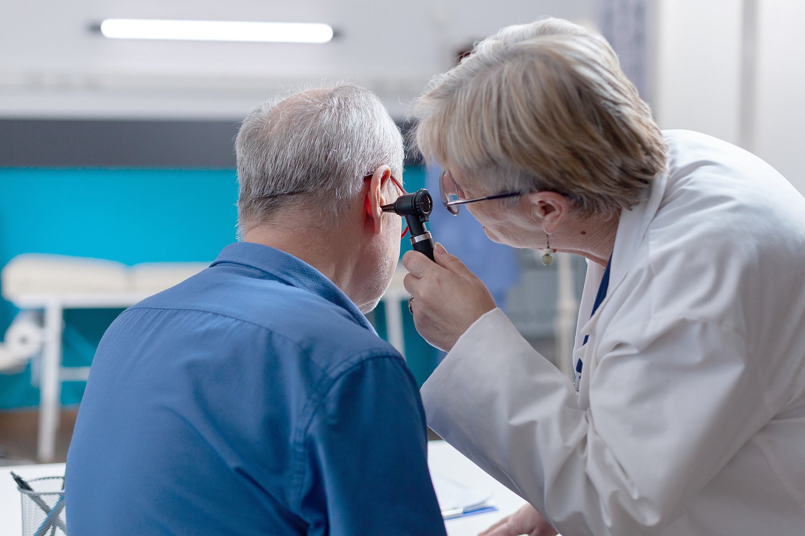 Physician holding otoscope to do ear consultation for patient at checkup visit. Woman doctor using otology instrument to examine infection and give medical advice to senior man.