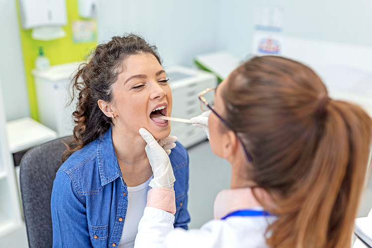 Female patient opening her mouth for the doctor to look in her throat. Otolaryngologist examines sore throat of patient.