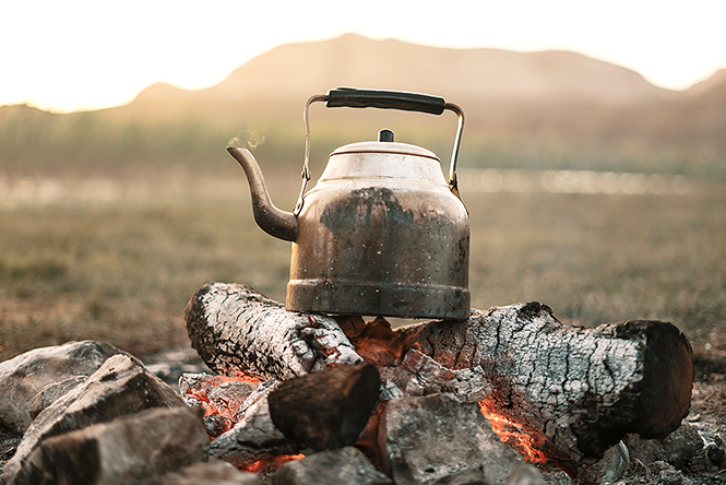 Close up Old kettle heated on a bonfire on a green mountain meadow. Epic travel in the mountains.